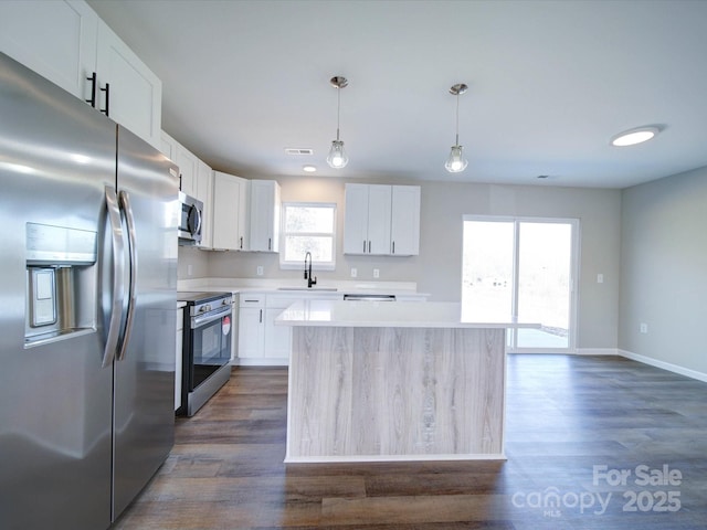 kitchen featuring appliances with stainless steel finishes, sink, white cabinetry, a kitchen island, and decorative light fixtures