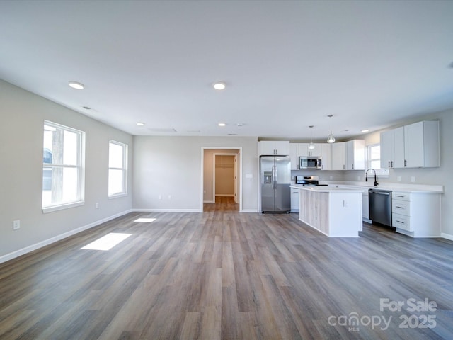 kitchen with light wood-type flooring, stainless steel appliances, hanging light fixtures, a center island, and white cabinets