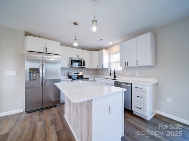 kitchen featuring appliances with stainless steel finishes, sink, a kitchen island, decorative light fixtures, and white cabinets