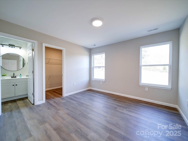 unfurnished bedroom featuring light wood-type flooring, sink, a closet, a spacious closet, and ensuite bathroom