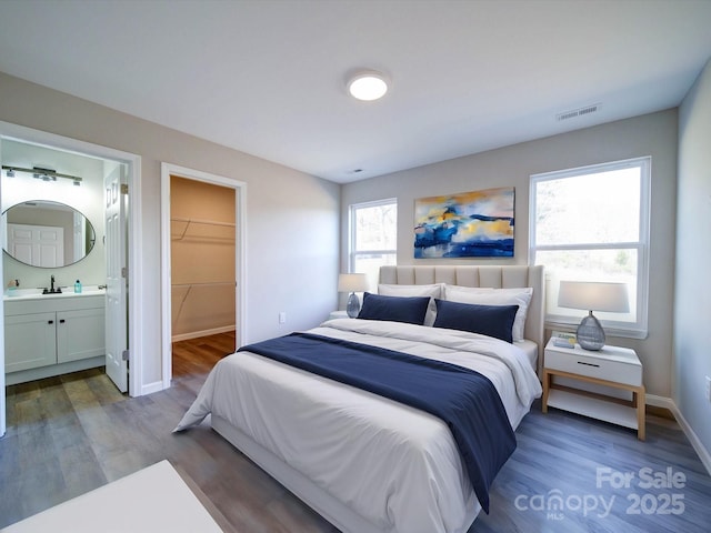 bedroom featuring sink, ensuite bathroom, dark hardwood / wood-style floors, and a walk in closet