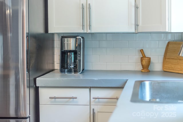 details featuring tasteful backsplash, stainless steel fridge, and white cabinets