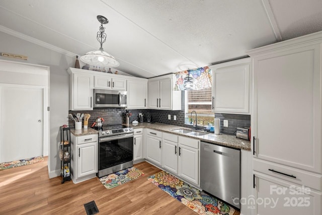 kitchen featuring sink, white cabinetry, vaulted ceiling, appliances with stainless steel finishes, and pendant lighting