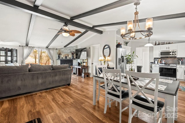 dining space with a stone fireplace, vaulted ceiling with beams, ceiling fan with notable chandelier, and light hardwood / wood-style flooring