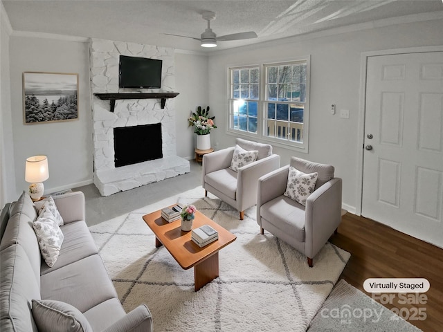 living room with ceiling fan, a fireplace, hardwood / wood-style floors, a textured ceiling, and ornamental molding