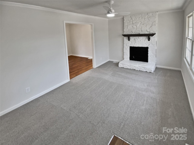 unfurnished living room with crown molding, carpet floors, a stone fireplace, and ceiling fan