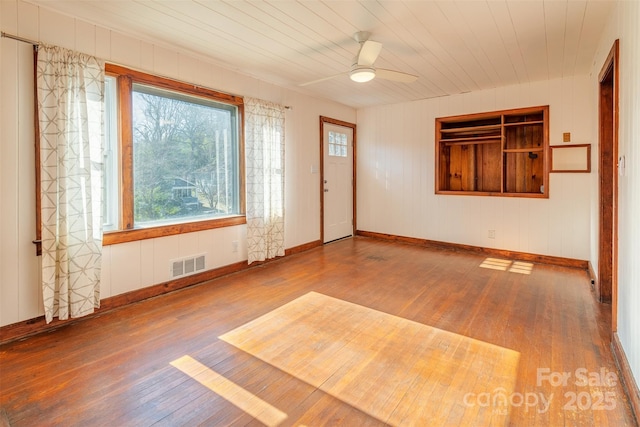 empty room with baseboards, visible vents, wooden ceiling, ceiling fan, and wood finished floors