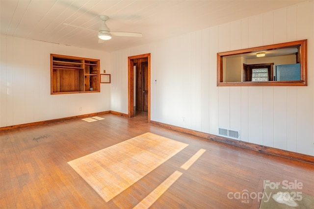 empty room with light wood-style floors, ceiling fan, visible vents, and baseboards