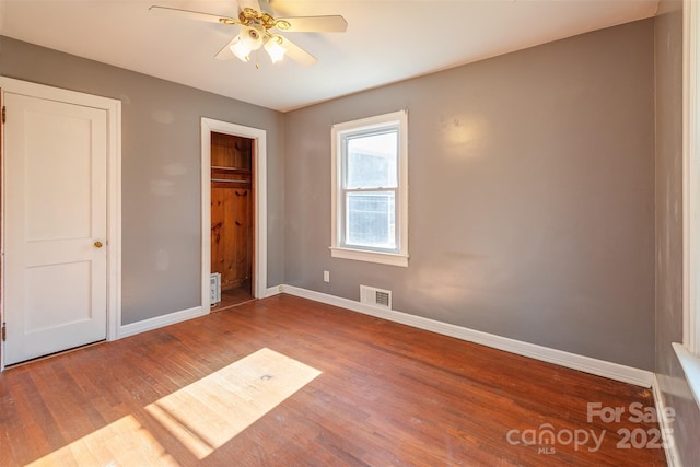 unfurnished bedroom with a ceiling fan, wood finished floors, visible vents, and baseboards