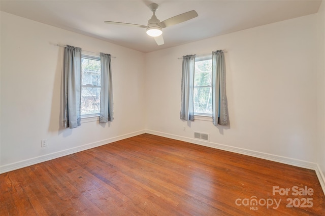 unfurnished room with a ceiling fan, visible vents, baseboards, and wood finished floors