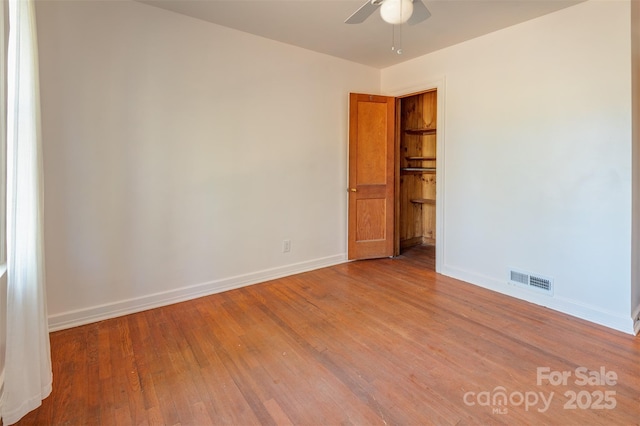 spare room with a ceiling fan, wood finished floors, visible vents, and baseboards