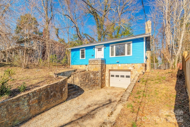 view of front of house featuring a garage, fence, dirt driveway, stone siding, and a chimney