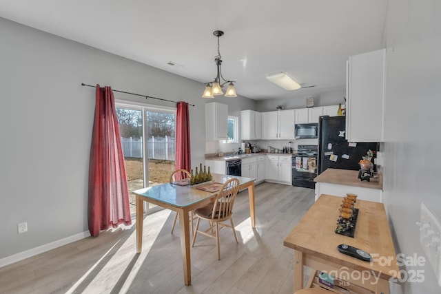 kitchen with hanging light fixtures, backsplash, black appliances, white cabinets, and light wood-type flooring