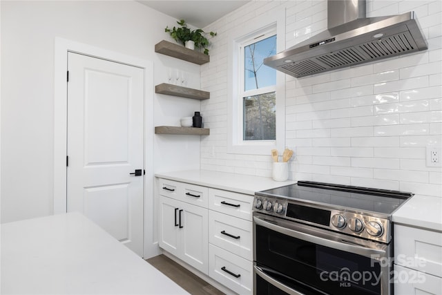 kitchen featuring backsplash, wall chimney exhaust hood, range with two ovens, and white cabinetry