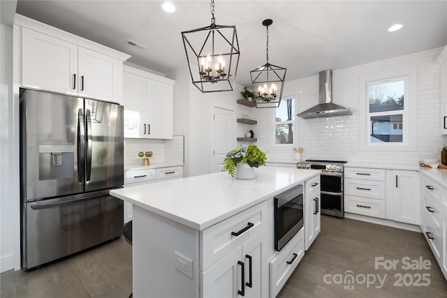 kitchen with white cabinetry, appliances with stainless steel finishes, tasteful backsplash, wall chimney range hood, and pendant lighting