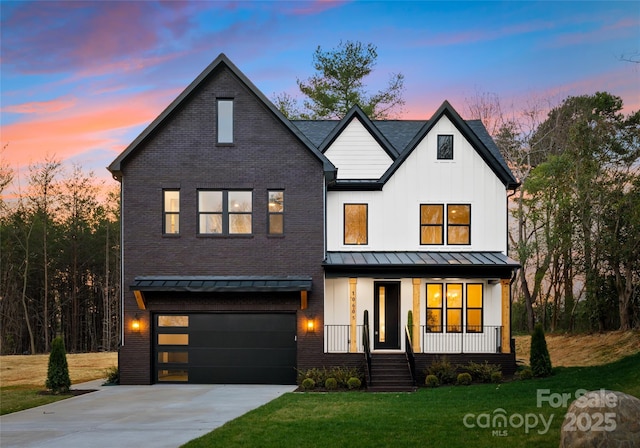 modern inspired farmhouse with a standing seam roof, covered porch, concrete driveway, a garage, and a lawn