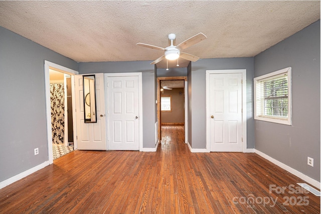 unfurnished bedroom with a textured ceiling, ceiling fan, dark wood-type flooring, and multiple windows