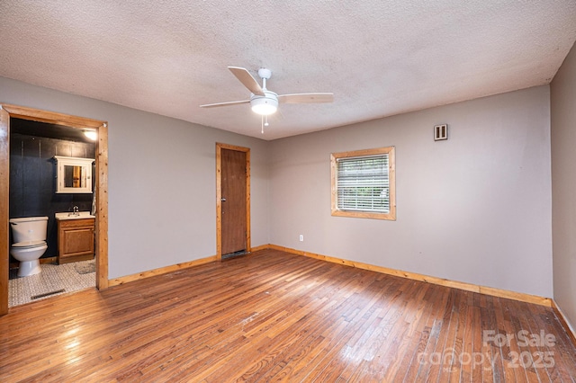 unfurnished bedroom with ceiling fan, ensuite bath, wood-type flooring, and a textured ceiling