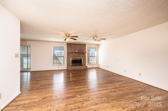 unfurnished living room featuring a fireplace, a wealth of natural light, dark wood-type flooring, and ceiling fan