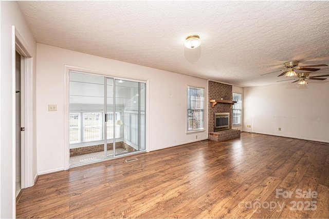 unfurnished living room with dark wood-type flooring, ceiling fan, a healthy amount of sunlight, and a fireplace