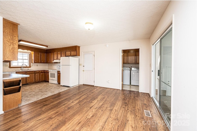 kitchen with washing machine and clothes dryer, sink, a textured ceiling, light wood-type flooring, and white appliances