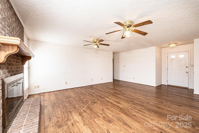 unfurnished living room with ceiling fan, a brick fireplace, dark hardwood / wood-style floors, and a textured ceiling