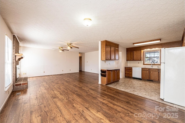 kitchen featuring sink, white appliances, ceiling fan, dark hardwood / wood-style flooring, and a brick fireplace