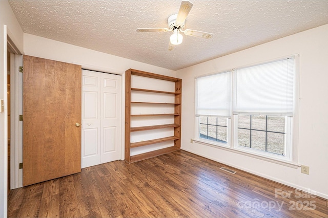 unfurnished bedroom with ceiling fan, dark hardwood / wood-style flooring, a closet, and a textured ceiling