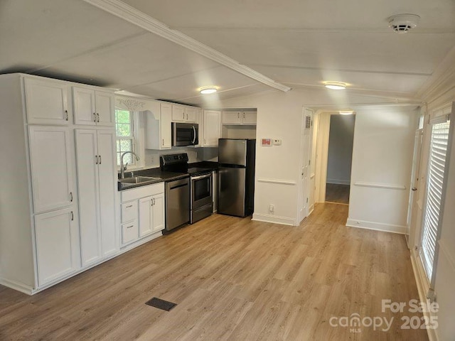 kitchen featuring appliances with stainless steel finishes, sink, white cabinets, light wood-type flooring, and lofted ceiling