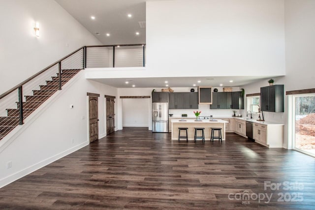 kitchen with appliances with stainless steel finishes, a kitchen breakfast bar, dark hardwood / wood-style flooring, a towering ceiling, and a center island