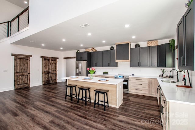 kitchen with wall chimney range hood, a kitchen island, sink, a breakfast bar area, and stainless steel appliances