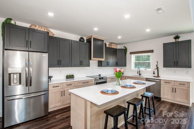 kitchen with stainless steel appliances, light brown cabinetry, a kitchen bar, and a kitchen island