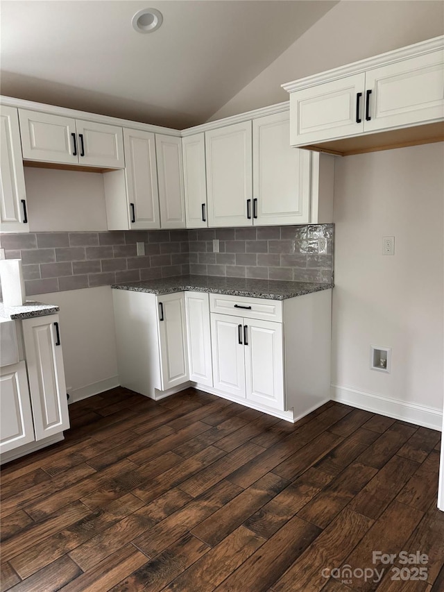 kitchen with white cabinetry, decorative backsplash, dark wood-type flooring, lofted ceiling, and dark stone countertops