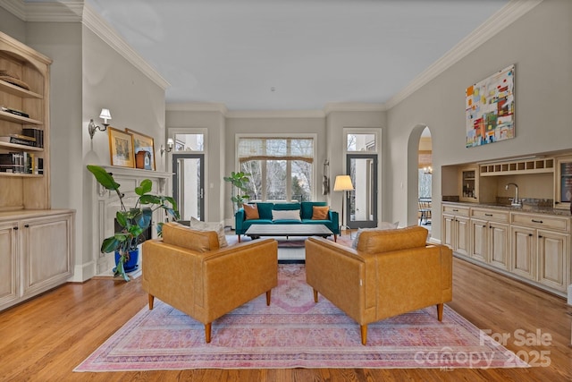 living area with arched walkways, light wood finished floors, ornamental molding, and baseboards