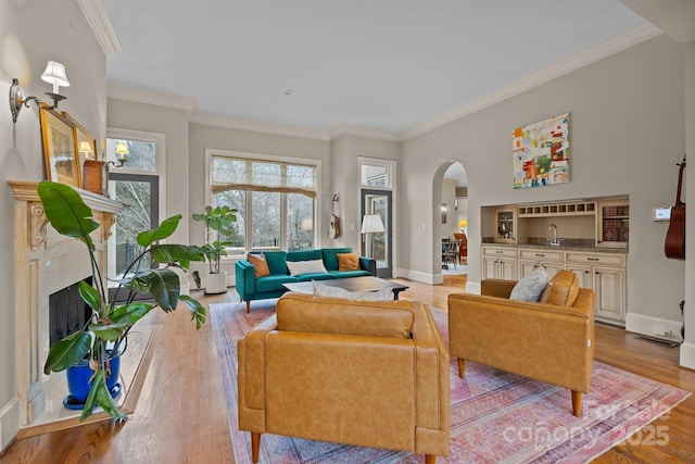 living room featuring arched walkways, a premium fireplace, baseboards, light wood-type flooring, and crown molding