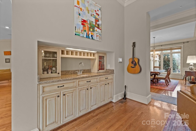 bar with crown molding, a sink, a notable chandelier, and light wood-style floors