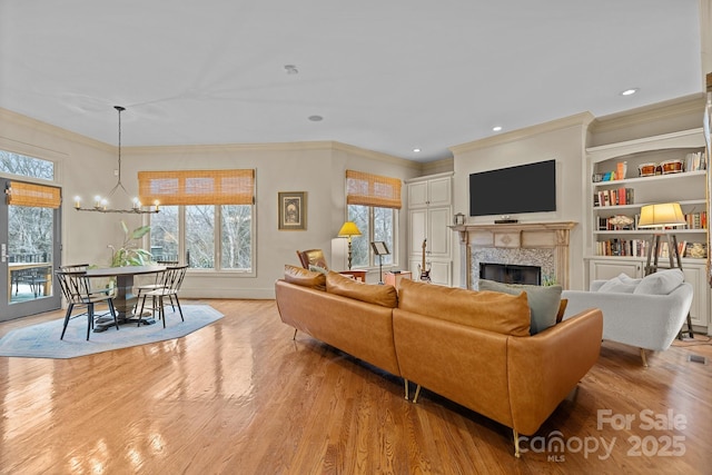 living area with a premium fireplace, ornamental molding, light wood-type flooring, a notable chandelier, and recessed lighting