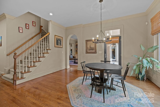 dining space featuring arched walkways, wood finished floors, stairs, and crown molding