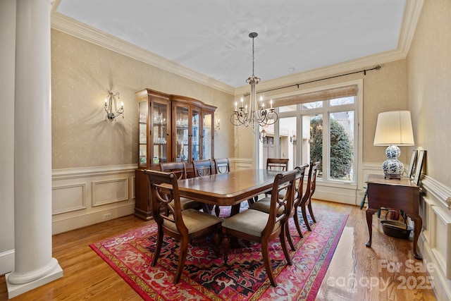 dining room featuring a chandelier, a wainscoted wall, light wood-style floors, decorative columns, and crown molding