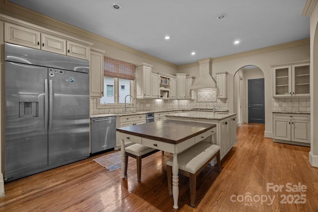 kitchen featuring arched walkways, stainless steel appliances, wood finished floors, a sink, and custom range hood