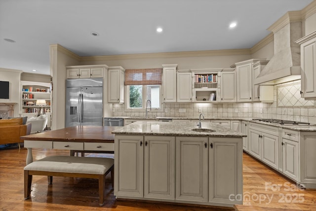 kitchen with light stone counters, stainless steel appliances, light wood-style floors, a sink, and premium range hood