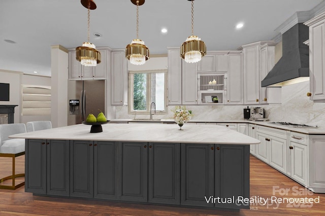 kitchen featuring stainless steel fridge with ice dispenser, a spacious island, wall chimney exhaust hood, a breakfast bar area, and a sink