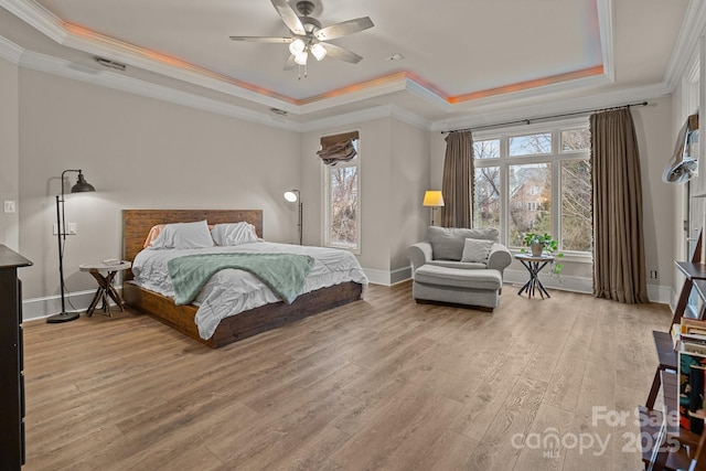 bedroom featuring a raised ceiling, light wood-style flooring, ornamental molding, ceiling fan, and baseboards