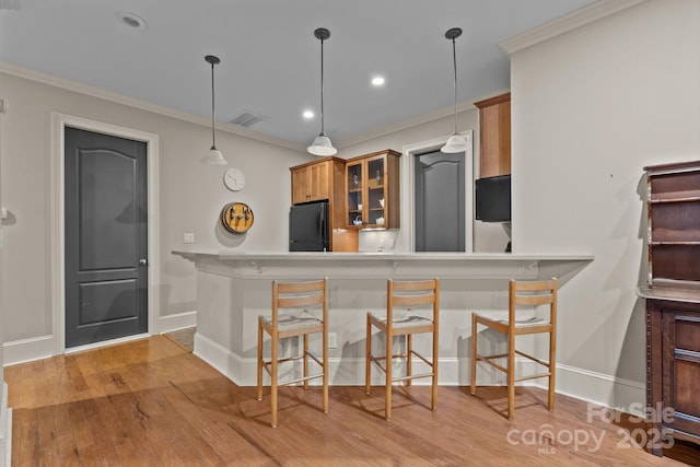 kitchen with brown cabinetry, freestanding refrigerator, visible vents, and crown molding