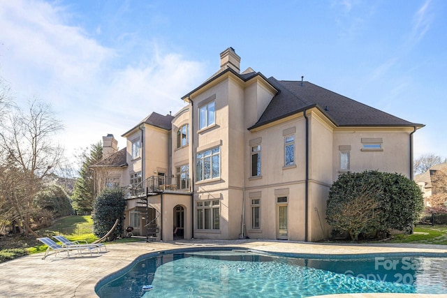 rear view of property with a patio area, an outdoor pool, a chimney, and stucco siding