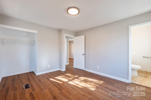 unfurnished bedroom with hardwood / wood-style flooring, ensuite bathroom, and a closet