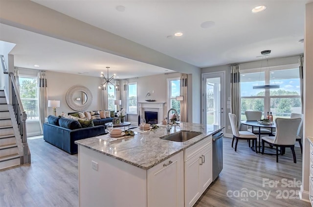 kitchen with light stone counters, a sink, white cabinetry, open floor plan, and a center island with sink