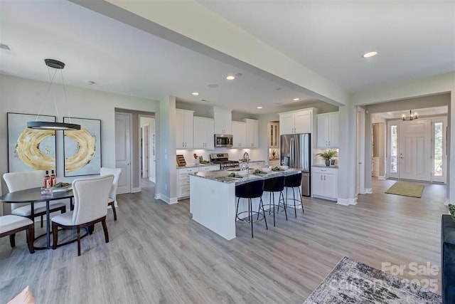 kitchen with pendant lighting, stainless steel appliances, a center island with sink, and white cabinets