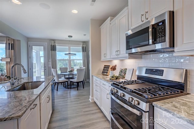 kitchen with light stone counters, stainless steel appliances, tasteful backsplash, white cabinetry, and a sink