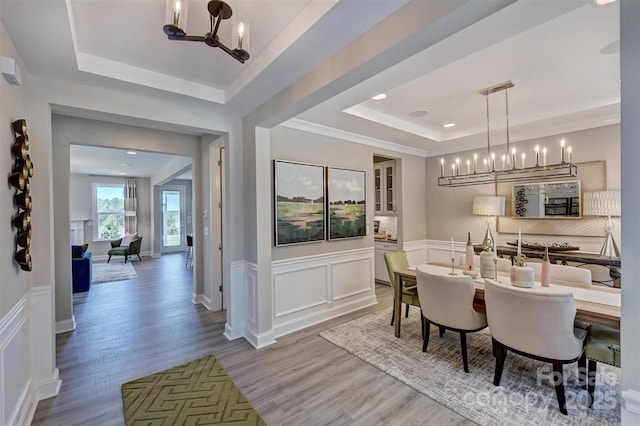 dining space with a wainscoted wall, wood finished floors, a tray ceiling, a decorative wall, and a notable chandelier